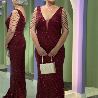 Mulher com vestido longo bordô bordado em frente a espelho