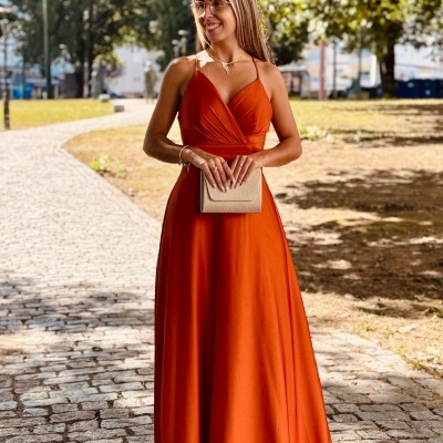 Vestido longo laranja de mulher com alças finas e mala bege em parque
