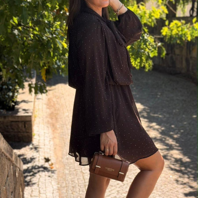 Mulher com vestido preto de pontos brancos e mala Valentino castanha ao ar livre