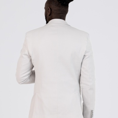 Homem de costas usando blazer branco com calças brancas num fundo branco