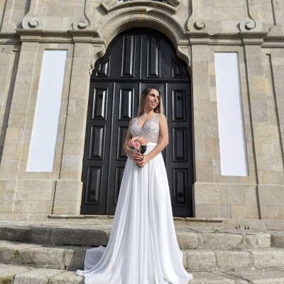 Mulher com vestido de noiva branco em frente a porta grande preta de madeira e fachada de pedra