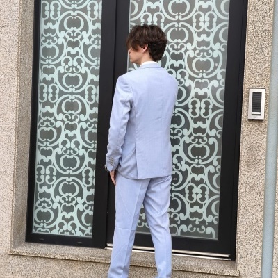 Homem com fato azul claro visto de costas em frente a porta decorativa