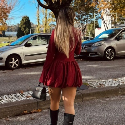 Mulher com vestido vermelho e botas pretas numa rua com carros estacionados e árvores de outono