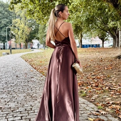 Vestido longo acetinado castanho chocolate com alças cruzadas e mala pequena dourada em passeio ao ar livre