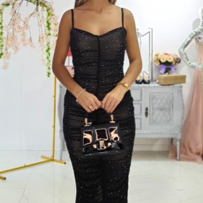 Mulher com vestido preto brilhante e mala preta em ambiente interior