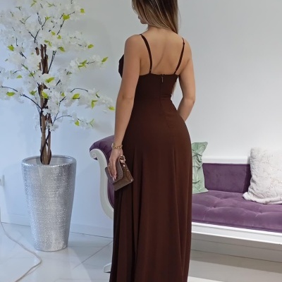 Mulher de costas com vestido longo castanho e acessório de mão sentado num ambiente interior moderno.