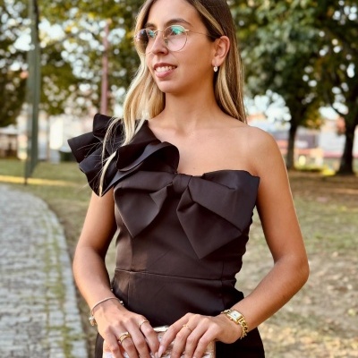 Mulher com vestido preto e mala clutch creme segurando ao ar livre