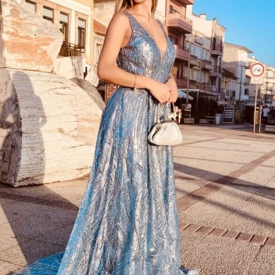 Mulher com vestido azul claro comprido e brilhante numa rua com edifícios.