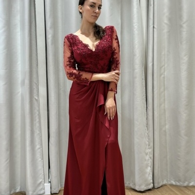 Mulher com vestido longo vermelho com mangas de tule bordado em ambiente com cortinas cinzentas.