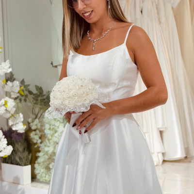 Mulher com vestido de noiva branco acetinado e bouquet de rosas brancas em loja