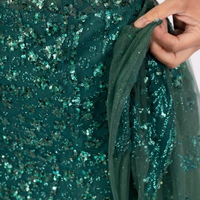 Detalhe de vestido verde com lantejoulas e tule, mão segurando o tecido