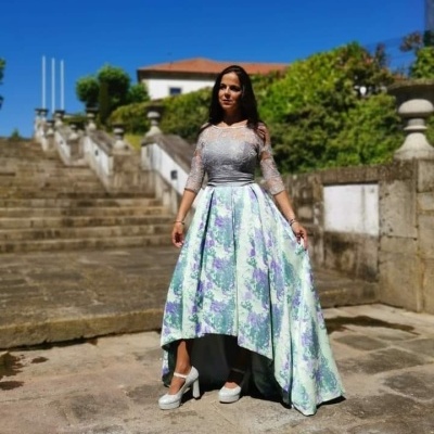 Vestido de festa com corpete de renda cinzenta e saia floral assimétrica, sapatos brancos, ao ar livre com escadas e plantas