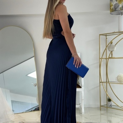 Mulher com vestido longo azul escuro e clutch azul num ambiente interior moderno