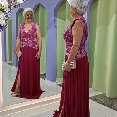 Mulher com vestido longo bordeaux com padrão tie-dye em frente a espelho decorado com flores roxas e brancas