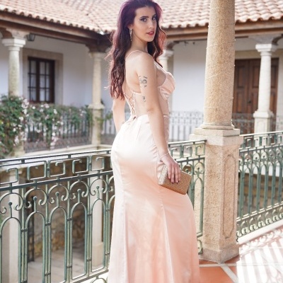 Mulher de vestido comprido cor de rosa claro segurando clutch dourada numa varanda antiga