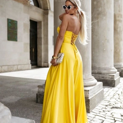 Vestido longo amarelo com amarração nas costas e acessórios em cenário com colunas de pedra