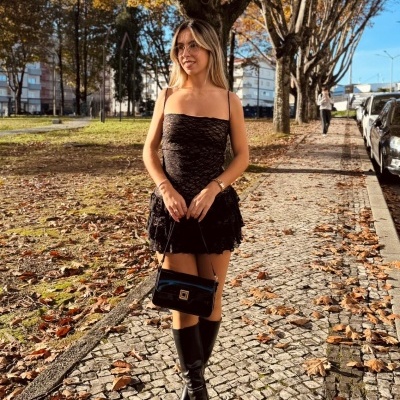 Mulher de vestido e botas pretas com mala a passear em calçada portuguesa com folhas.