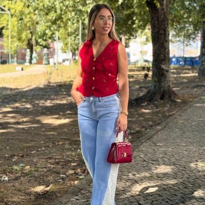 Mulher com colete vermelho e calças de ganga bicolores numa calçada de parque