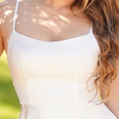 Vestido branco com alças finas e tecido liso usado por mulher ao ar livre