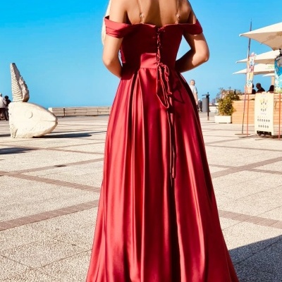 Vestido comprido vermelho acetinado com fecho tipo corset nas costas, usado por mulher de costas ao ar livre