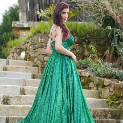 Vestido longo verde metálico com alças finas, em escadas exteriores com muro de pedra e plantas