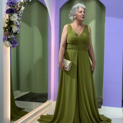 Senhora com vestido verde longo e mala de mão bege em ambiente com parede lilás e espelho decorado