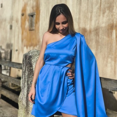 Vestido azul cintilante assimétrico com detalhe fluído usado por mulher num ambiente externo