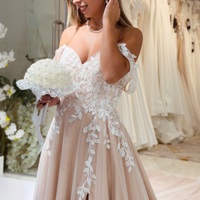 Mulher com vestido de noiva nude com bordados florais brancos e bouquet de rosas brancas