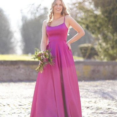 Vestido longo rosa vibrante com alças finas, tecido brilhante, mulher com ramo flores ao ar livre