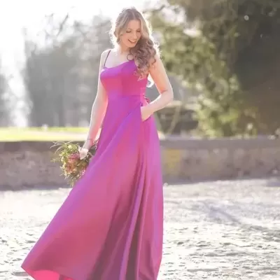 Mulher de vestido longo fúcsia segurando flores em ambiente exterior