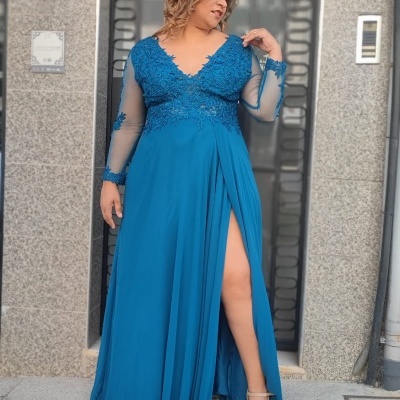 Mulher com vestido comprido azul de renda e manga comprida, junto a porta metálica