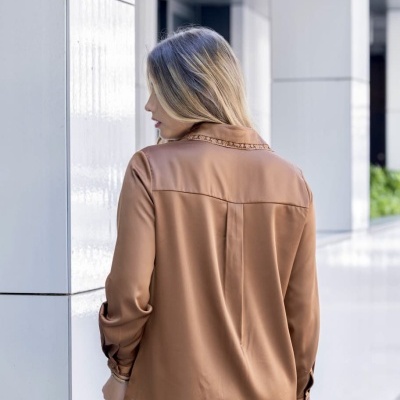 Mulher vista de costas com blusa castanha de manga comprida e calças brancas