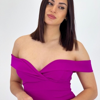 Modelo veste vestido rosa ombro a ombro com decote cruzado e segura carteira bege texturizada.