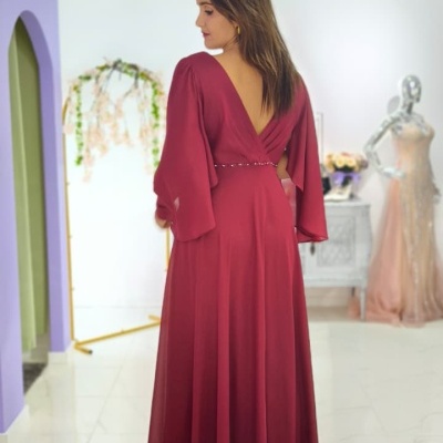 Vestido longo bordô com mangas amplas e decote em V nas costas numa loja de roupa.