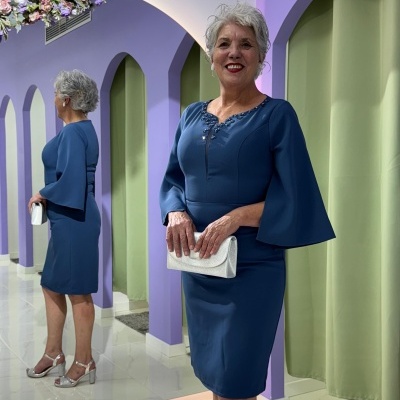 Mulher com vestido azul e carteira branca num ambiente moderno com parede roxa e cortinas verdes