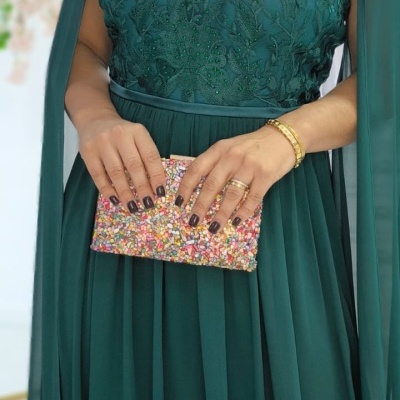 Vestido verde com bordados e transparência segurando carteira colorida