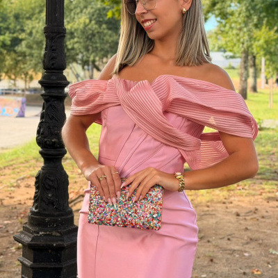 Mulher em vestido rosa com clutch colorida e óculos em parque