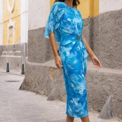 Vestido midi azul com padrão abstrato, cinto com fivela e salto alto dourado numa rua.