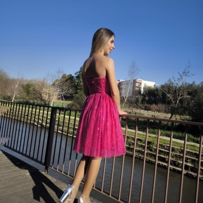 Mulher de vestido rosa cintilante e sapatos prateados num passadiço à beira de rio