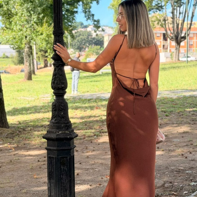 Mulher de costas com vestido castanho longo em parque com postes e árvores