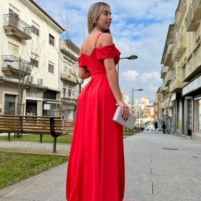 Mulher de vestido comprido vermelho com alças finas e folhos nos ombros numa calçada urbana