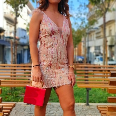 Mulher com vestido cor de rosa com padrões, sandálias bege e bolsa vermelha num parque urbano