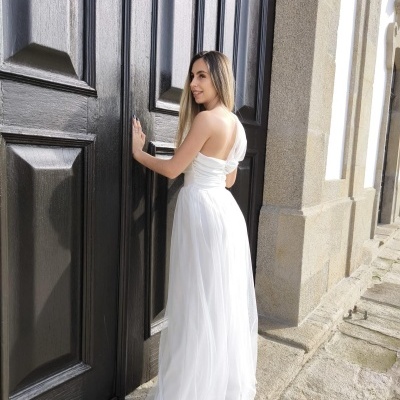 Mulher com vestido longo branco junto a porta preta de madeira