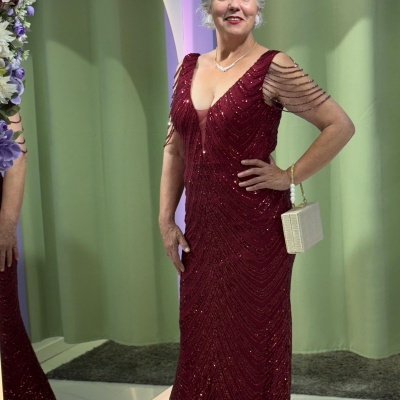 Mulher com vestido vermelho longo brilhante e bolsa branca em ambiente interior com espelho