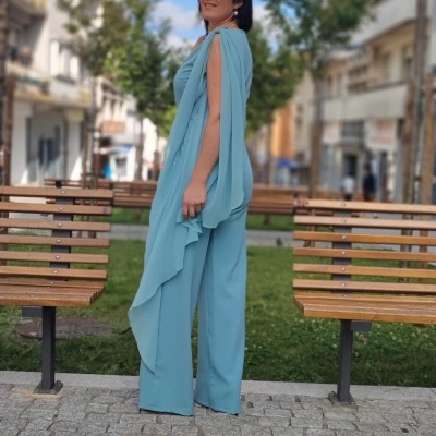 Mulher em fato azul claro com calças largas e blusa fluida, usando óculos escuros, em rua com bancos de madeira e árvores.
