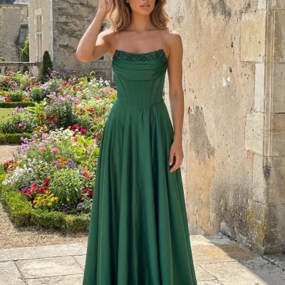 Vestido longo verde esmeralda com corpete e lantejoulas, exterior com flores e parede de pedra