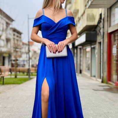 Mulher de vestido longo azul com fenda e mala prateada numa rua