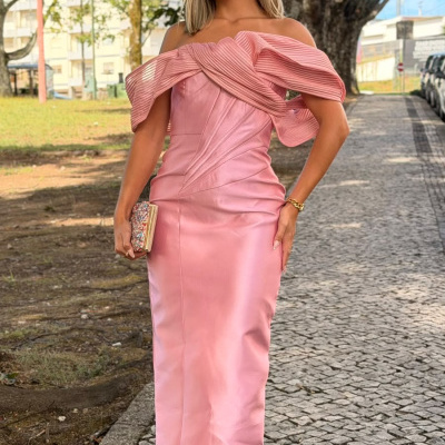 Mulher com vestido comprido rosa claro e clutch numa calçada exterior
