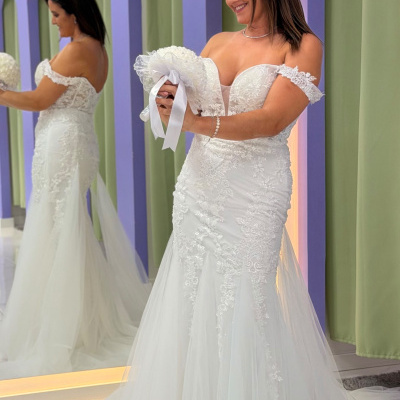 Mulher com vestido de noiva branco rendado e bouquet em ambiente interior com parede lilás e verde