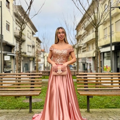 Mulher com vestido de festa rosa claro bordado e saia acetinada em rua urbana entre bancos de madeira